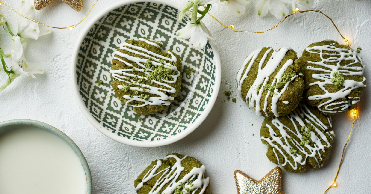 Vivid green matcha cookies drizzled with white icing on a green-and-white geometric bowl, with matcha latte, string lights, and a gold star ornament.