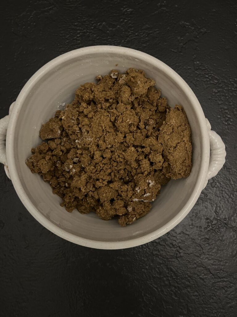 Overhead view of a white mixing bowl filled with dark brown, shaggy gingerbread cookie dough that has just been combined.